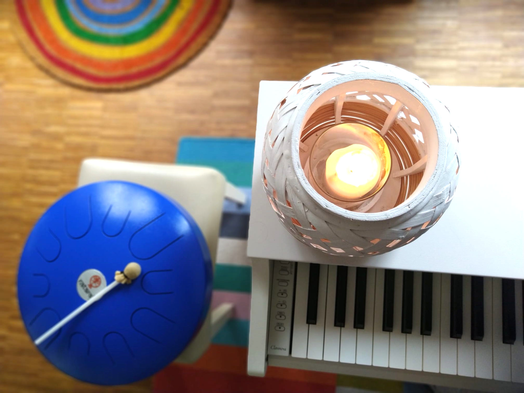 Photo of a blue steel tongue drum, piano and candle